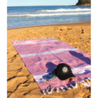 A pink beach towel, hat, and camera on sand near the ocean with waves in the background.