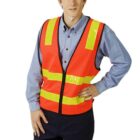 Person in a reflective orange safety vest and blue shirt standing with one hand on hip.