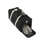 Black duffel bag with white straps, shoe compartment open showing a pair of gray sneakers.