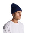 Man in a white shirt and blue beanie looking to the side against a white background.