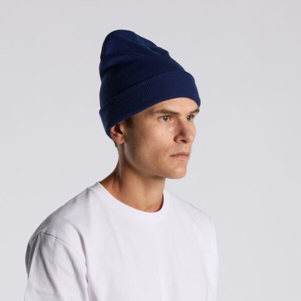 Person in a white shirt and blue beanie looks to the side against a plain background.