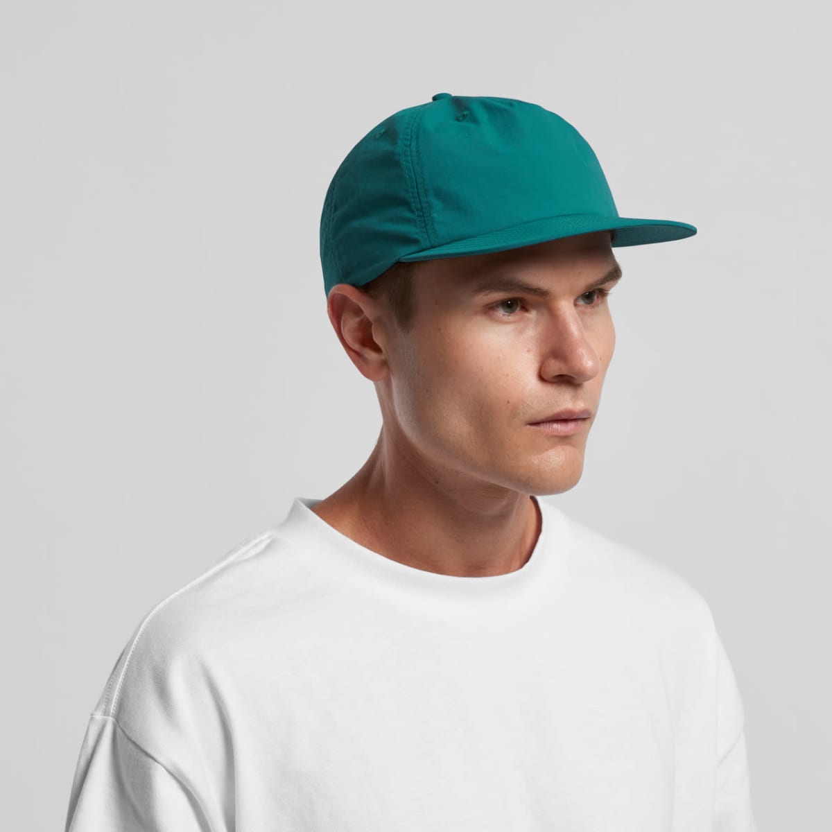 Man wearing a teal cap and white shirt looking to the side against a plain background.