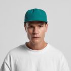 A man in a teal cap and white shirt looks straight at the camera against a gray background.