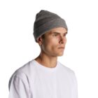 A man in a gray knit beanie and white t-shirt looks off to the side against a white background.