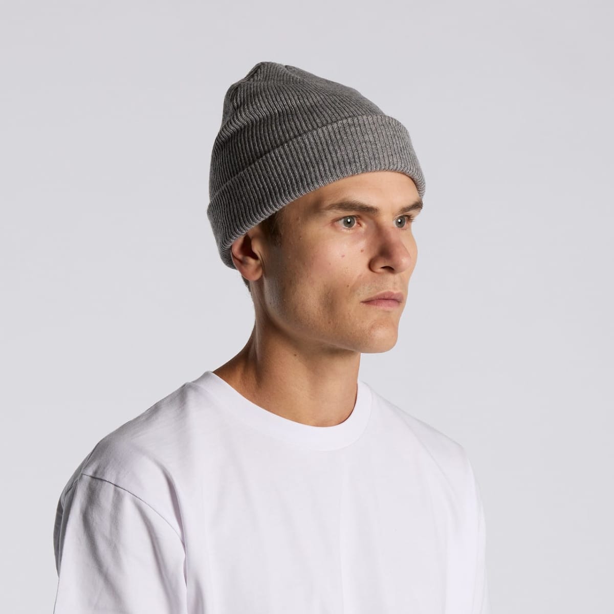 Man in a gray knit beanie and white shirt looking to the side against a plain background.