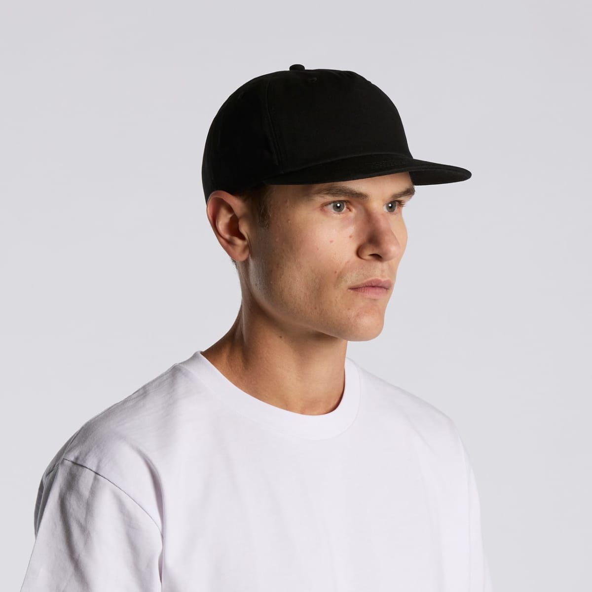 Man in a white shirt and black cap looking to the side against a plain background.