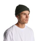 Man in a white shirt and green knit beanie looks to the side against a white background.