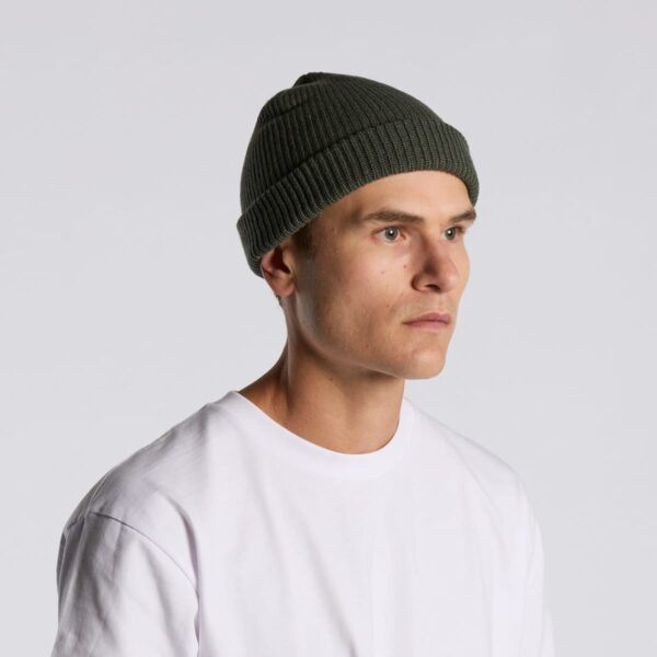 Man in a white t-shirt and green knit beanie looking to the side against a gray background.