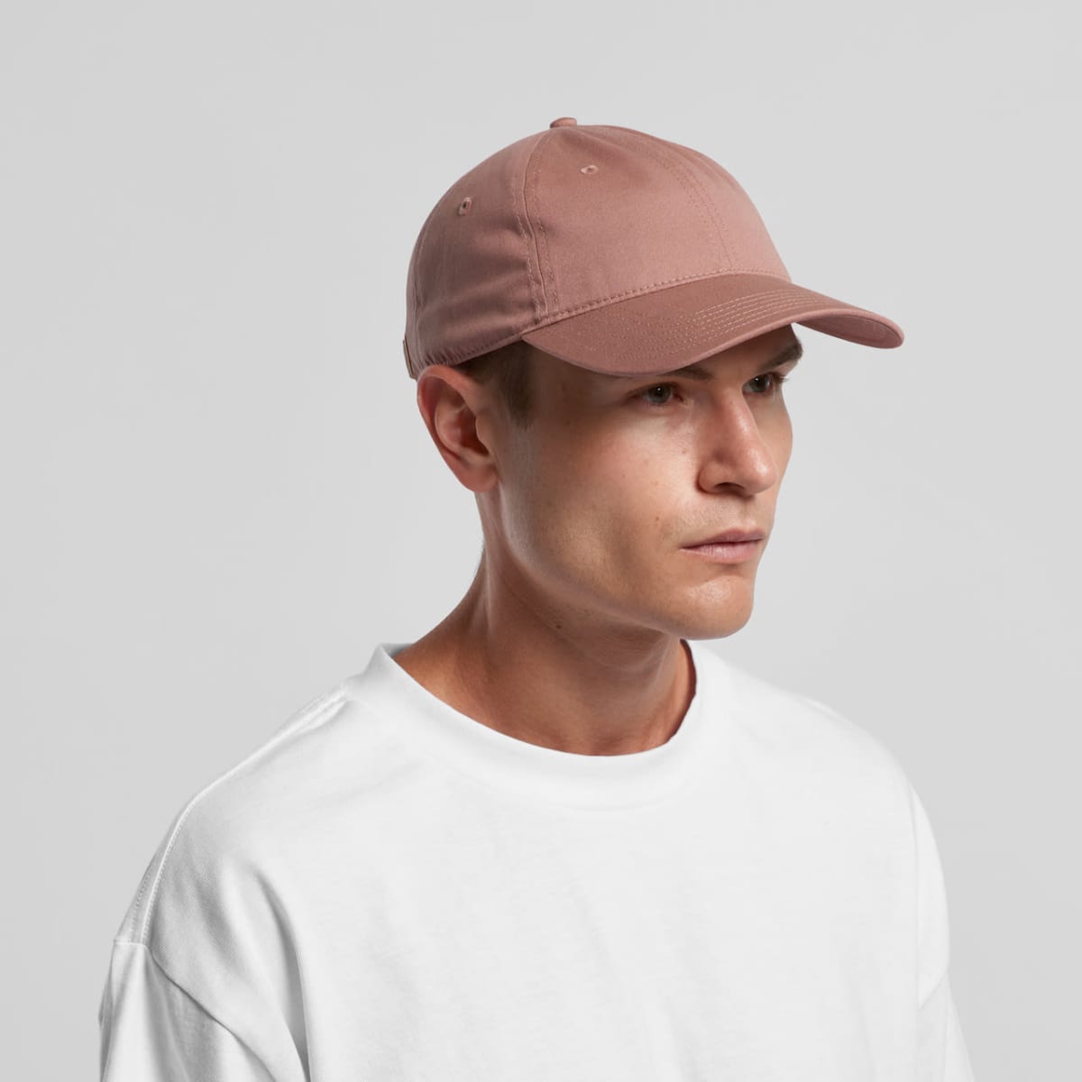 Person wearing a pink baseball cap and white shirt, looking to the side against a gray background.