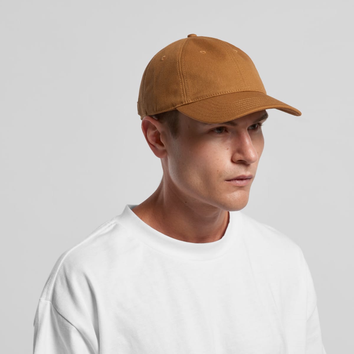 Man in a brown baseball cap and white shirt looking to the side against a plain background.