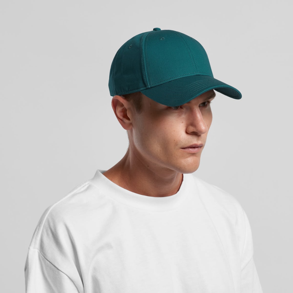 Person wearing a teal baseball cap and white t-shirt against a plain background.