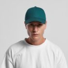 Man in a teal baseball cap and white t-shirt staring straight ahead against a plain background.