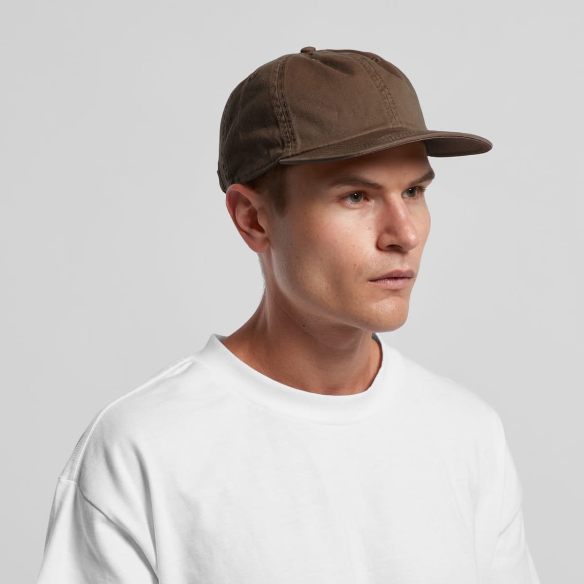 A man in a brown cap and white shirt looks to the side against a plain background.