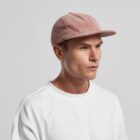 Man in a white shirt and pink corduroy cap looking to the side against a plain background.
