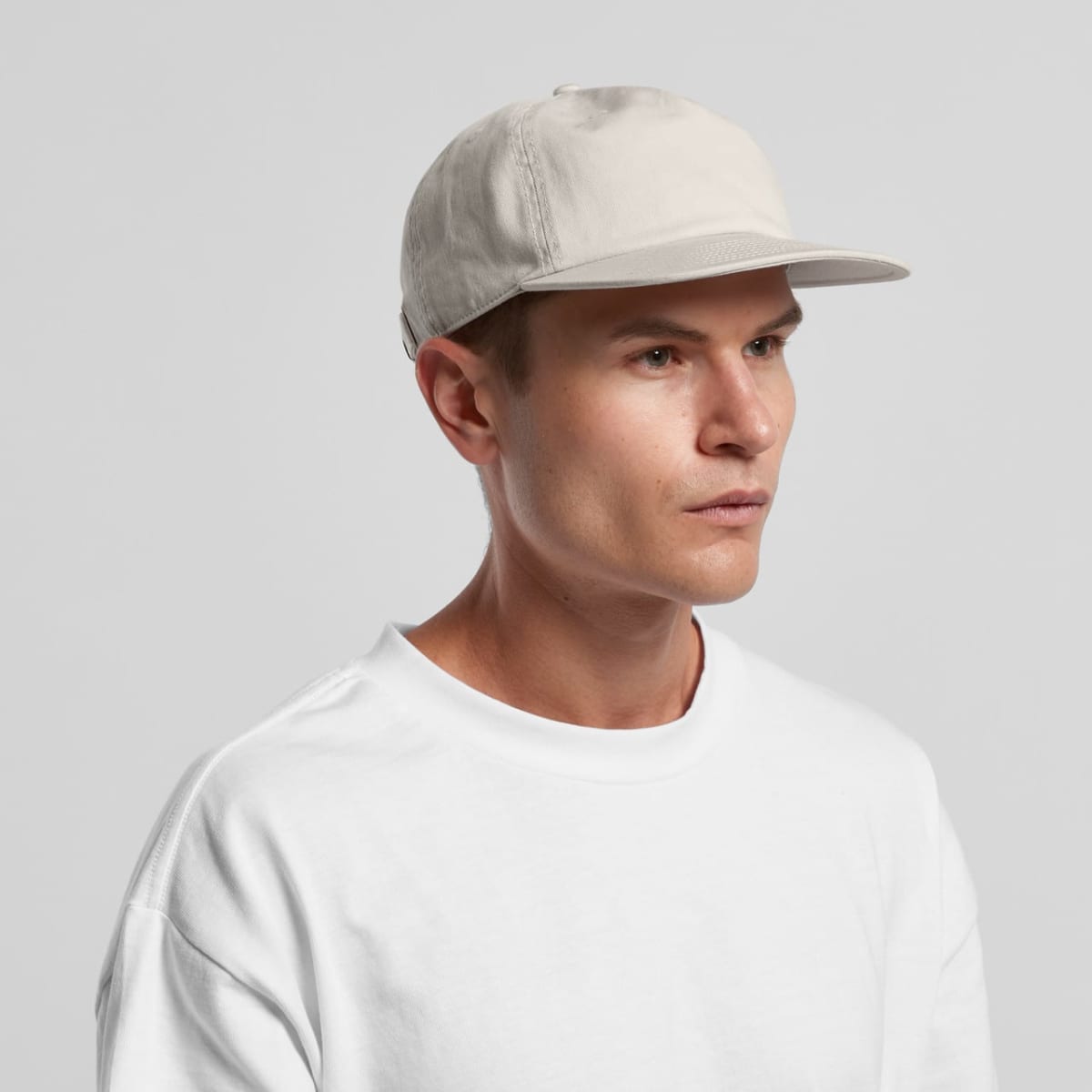 Man in a white shirt and beige cap looking to the side against a plain background.