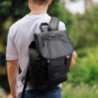 Person with black backpack outdoors, wearing a white shirt.