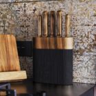 Wooden knife block with five knives on a kitchen counter, ornate patterned wall in background.