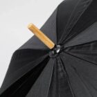 Close-up of a black umbrella with a wooden handle against a plain background.