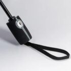 Close-up of a black handle with a wrist strap and silver button on a light background.