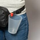 Person wearing jeans and a gray shirt with a black belt bag and a plastic cup holder attached.