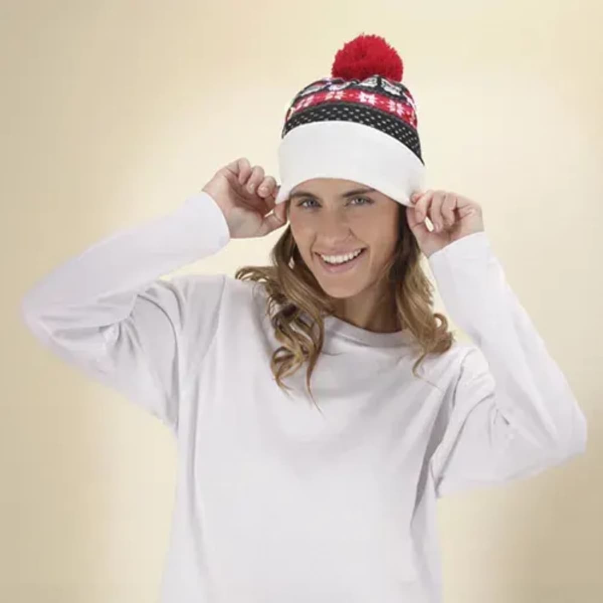 Woman in a white sweater smiling and adjusting a festive winter hat with a red pom-pom.