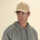 Man in a beige cap and gray hoodie looking to the side against a light background.