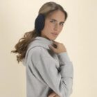 Woman in a gray hoodie wearing black earmuffs, posing against a beige background.