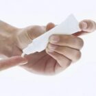 Hand squeezing cream from a white tube onto a fingertip, against a light background.