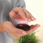 Hands warming over a small, round, black portable hand warmer device.