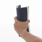 A hand holding and bending a closed, navy blue notebook against a white background.