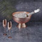 Copper ice bucket with champagne and two empty champagne flutes on a gray surface.