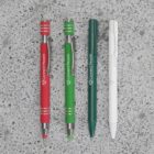 Four pens on a speckled surface: two red, one green, one white.