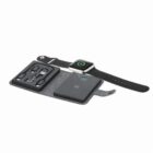 A black smartwatch charging on a wireless pad with various charging adapters beside it.