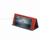 Smartphone charging and playing a video, propped up on a red and gray foldable stand.