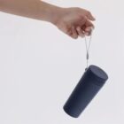 A hand holding a navy blue tumbler by its attached gray strap against a white background.