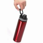 Hand holding a red water bottle by its black carabiner-style handle.