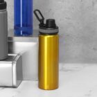 A metallic yellow water bottle with a black lid on a white and gray surface.