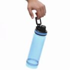 A hand holds a blue water bottle by its black lid loop.