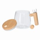 Clear glass teapot with wooden handle, lid, and a small wooden accessory beside it.