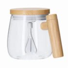 Clear glass pitcher with wooden lid and handle, and a metal whisk inside.