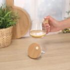 A hand lifts a glass mug with a wooden handle from a wooden table near a plant basket.
