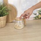 A hand pressing the lid of a glass jar with a wooden handle on a wooden table.