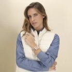 Woman in blue shirt and white vest poses, wearing a watch on her left wrist.