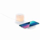 A phone charging wirelessly next to a small glowing lamp on a white surface.