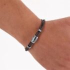 A brown cord bracelet with a silver charm on a persons wrist.