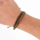 A wrist wearing three beaded and braided bracelets in black, green, and brown.