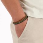 Person wearing a beige shirt and pants with hand in pocket, wearing three colorful bracelets.