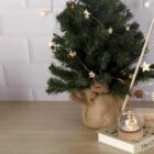 Mini Christmas tree with star lights and a snow globe on stacked books on a wooden table.