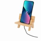 A smartphone charging on a small wooden stand shaped like a bench.