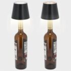 Two wine bottles with black lampshades on top, resembling table lamps.